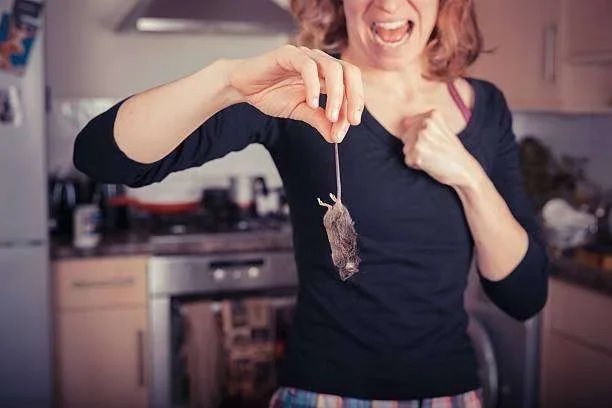 Mulher assustada segurando um rato morto pela cauda em uma cozinha